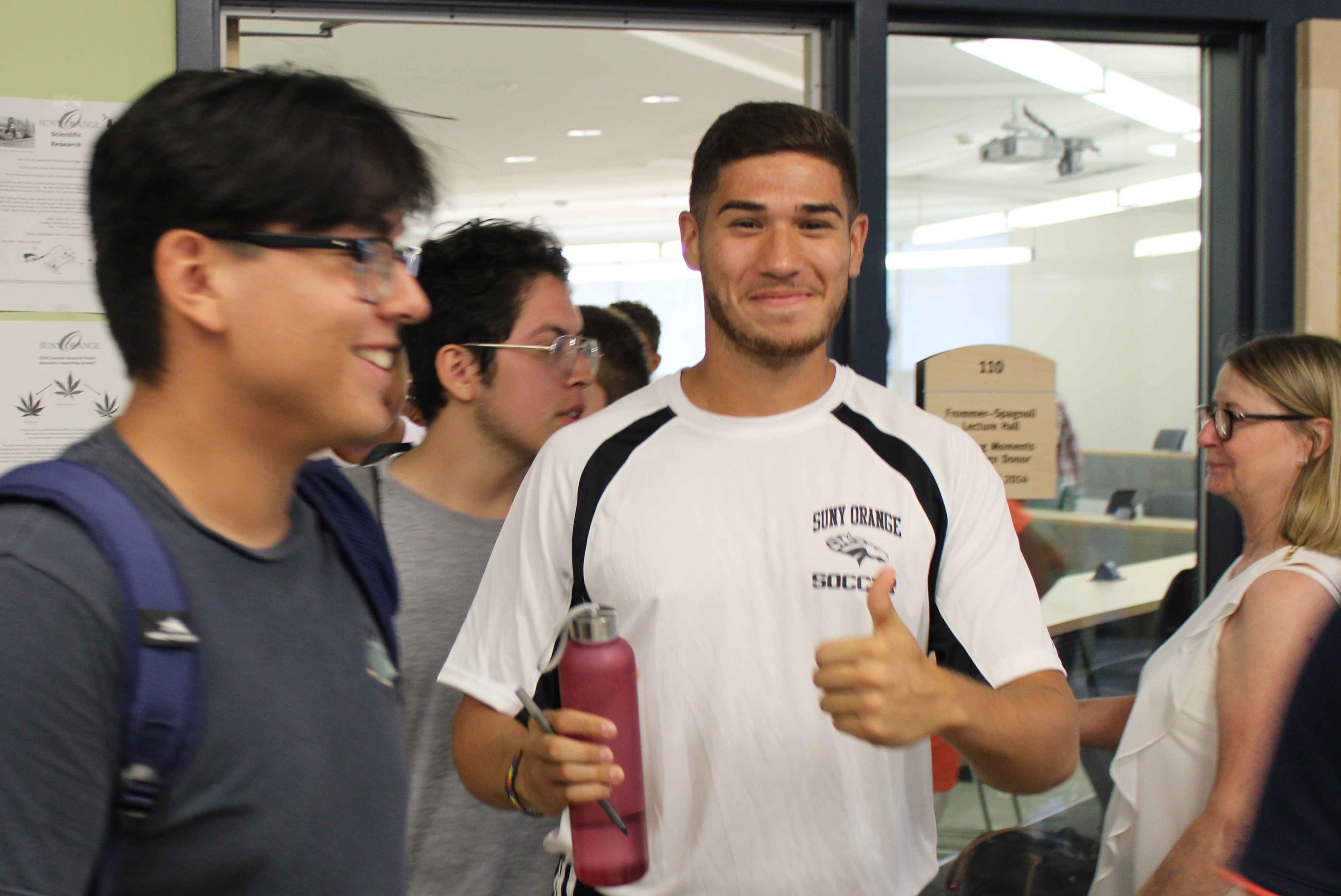 student giving thumbs up to camera in front of classroom