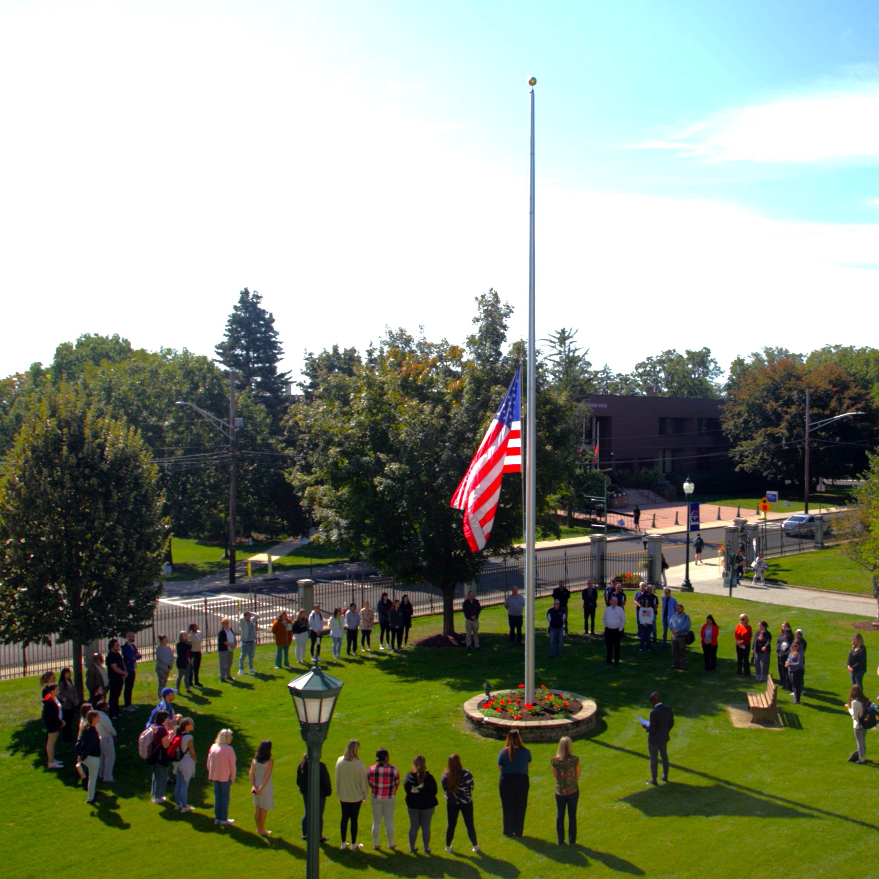 image of american flag at half mast with a circle of people surrounding from an overhead view
