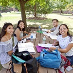 Photo: Three Female Students and One Male Student with Notebooks and Textbooks at a Campus Picnic Table