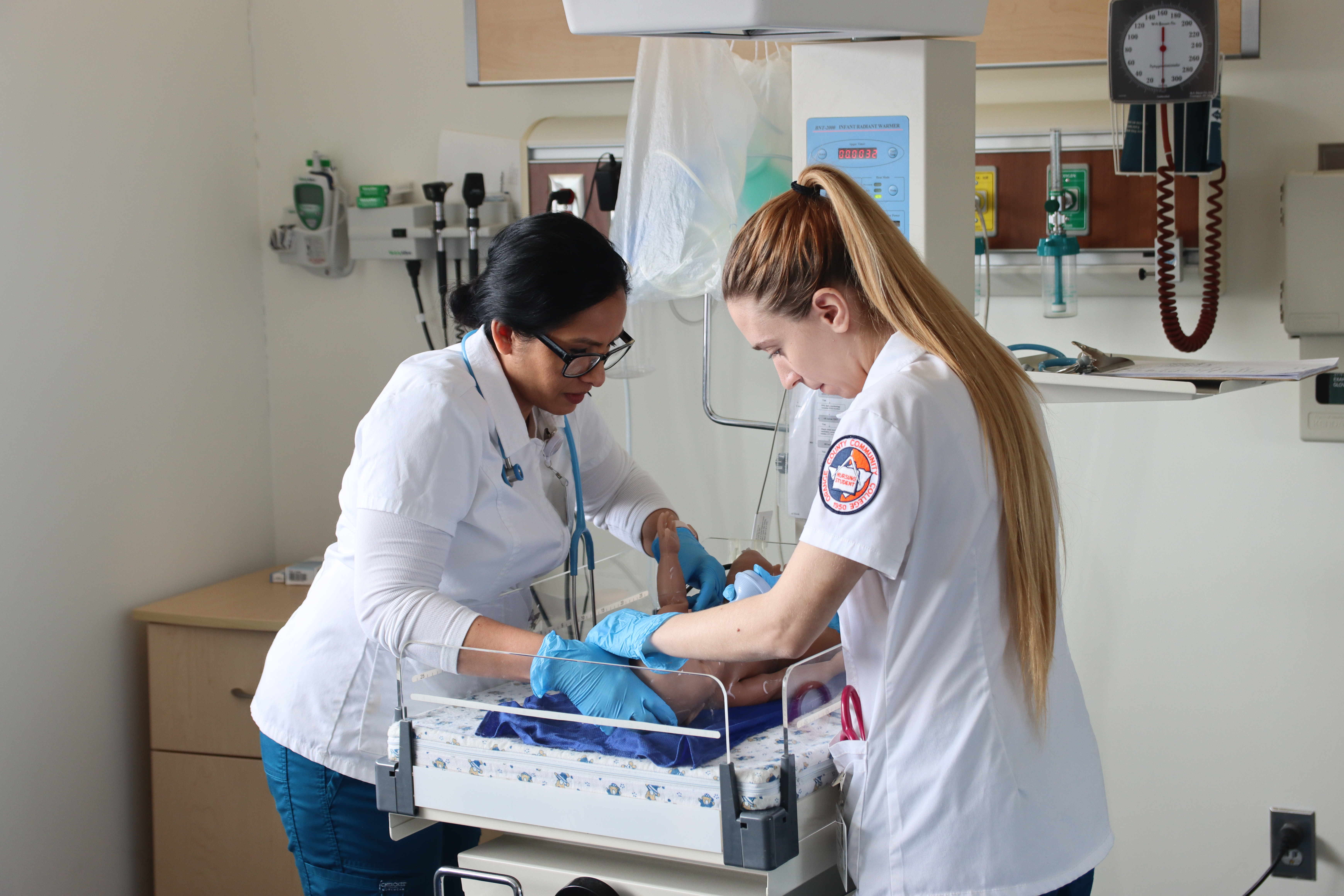 two nursing students leaning over a simulation mannequin baby